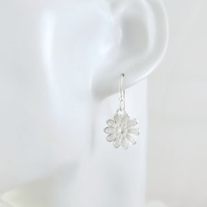 May include: Silver dangle earrings with a white flower design.