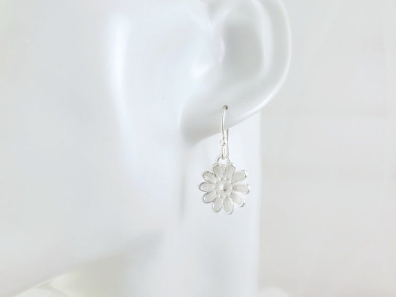 May include: Silver dangle earrings with a white flower design.
