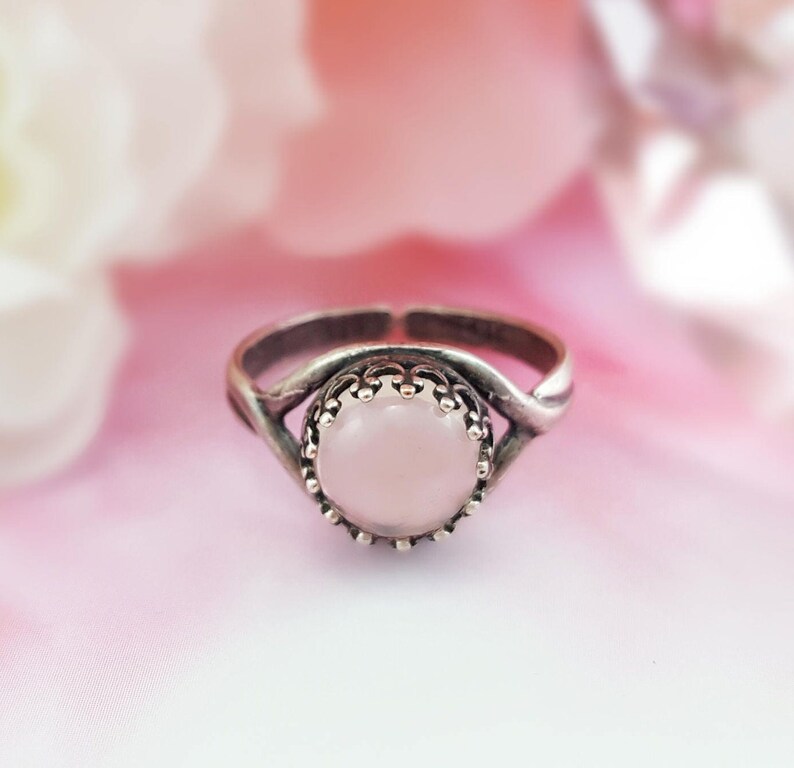 May include: A silver ring with a delicate twisted band and a round pink stone set in a crown-like bezel.