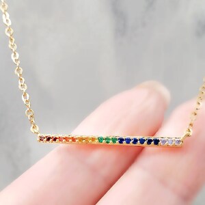 May include: A gold chain necklace with a thin bar pendant set with rainbow colored gemstones.