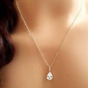 May include: A delicate gold-toned necklace featuring a teardrop-shaped pendant with a clear, sparkling gemstone. The pendant hangs from a fine chain, creating an elegant and understated look. The necklace is shown against a skin-toned background.