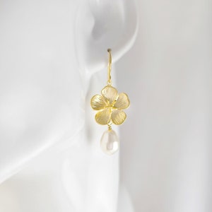 May include: Gold flower dangle earrings with a white pearl drop. The flower is textured and has a delicate design.