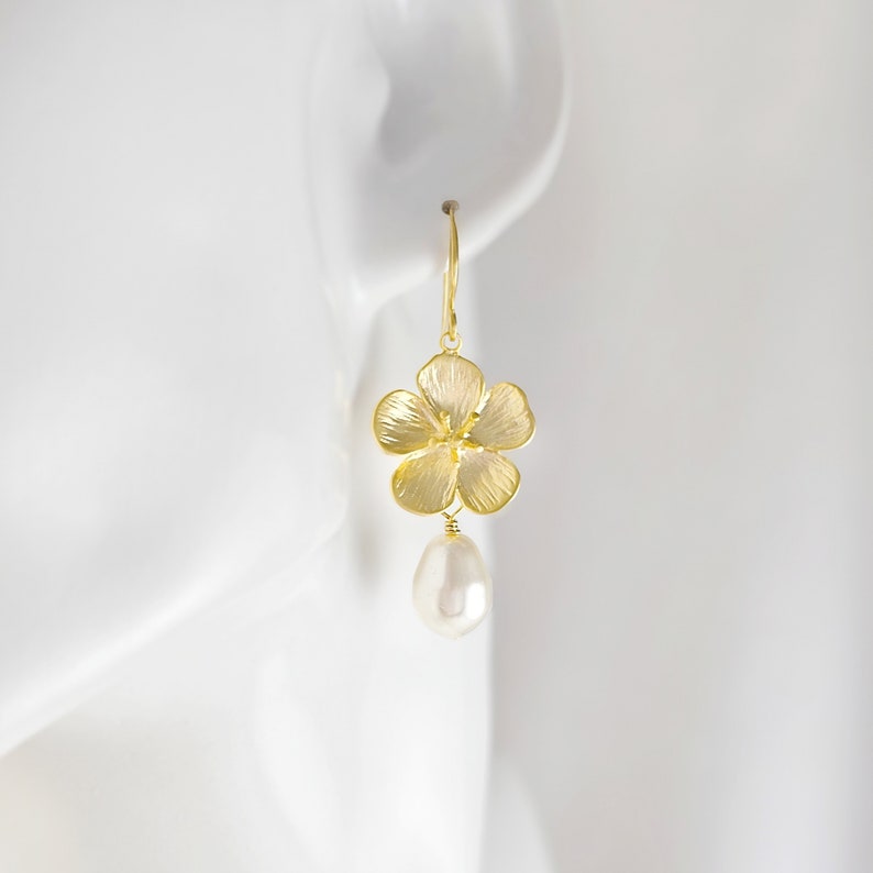 May include: Gold flower dangle earrings with a white pearl drop. The flower is textured and has a delicate design.