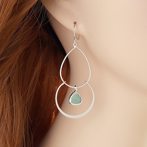 May include: Silver dangle earrings with a teardrop-shaped green gemstone pendant.