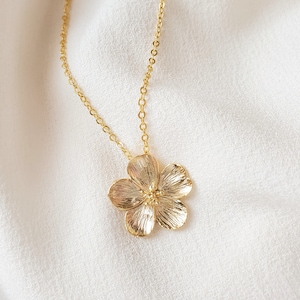 May include: A gold chain necklace with a delicate flower pendant. The flower is detailed and has a textured finish.