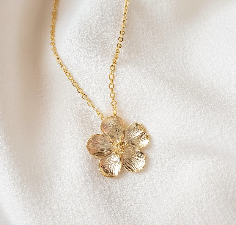 May include: A gold chain necklace with a delicate flower pendant. The flower is detailed and has a textured finish.