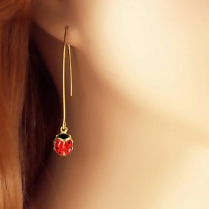May include: Gold dangle earrings with a red ladybug charm.
