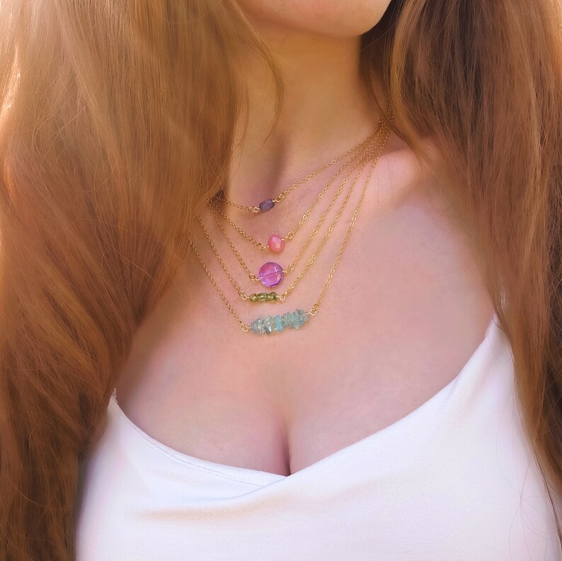 Puede incluir: Un collar de oro de varias capas con m&uacute;ltiples colgantes de piedras preciosas. El collar presenta un colgante de piedra preciosa rosa, morado y verde, as&iacute; como una barra de piedras preciosas azul claro.