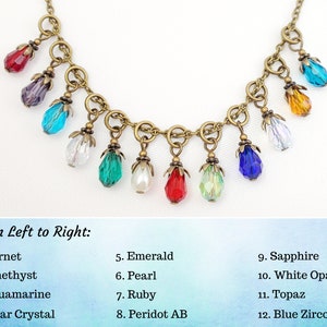 May include: A necklace with a bronze chain and twelve colorful teardrop-shaped pendants. The pendants include garnet, amethyst, aquamarine, clear crystal, emerald, pearl, ruby, peridot AB, sapphire, white opal, topaz, and blue zircon.