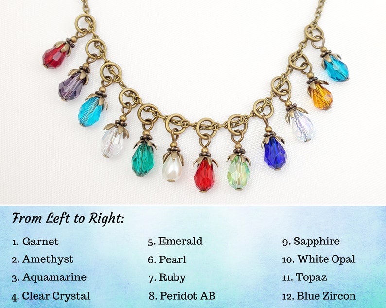 May include: A necklace with a bronze chain and twelve colorful teardrop-shaped pendants. The pendants include garnet, amethyst, aquamarine, clear crystal, emerald, pearl, ruby, peridot AB, sapphire, white opal, topaz, and blue zircon.