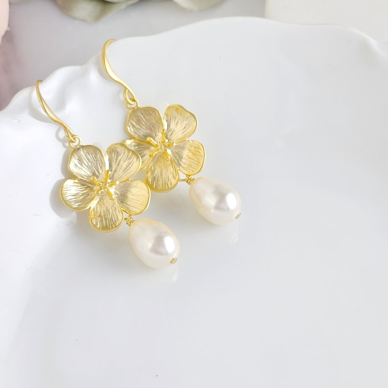 May include: Gold flower earrings with a pearl drop. The flowers are textured and have a delicate design.