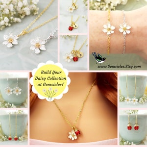 May include: A collection of delicate daisy jewelry, including necklaces, earrings, and bracelets. The jewelry features small white daisy charms with a gold or silver finish. Some pieces also include a small red ladybug charm. The image includes the text "Build Your Daisy Collection at Gemsicles!" and the website address "www.Gemsicles.Etsy.com".