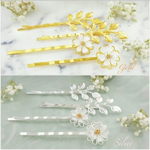 May include: Set of six gold and silver hair clips with a floral design. Each clip features a delicate white flower with a gold center and a leafy branch. The clips are arranged in two rows, with the gold clips on top and the silver clips on the bottom. The text "Gold" and "Silver" is visible below the clips.
