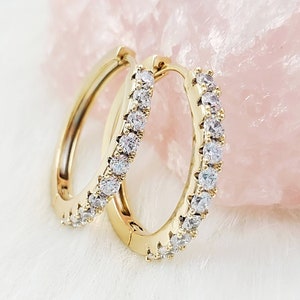 May include: A pair of gold hoop earrings with a row of clear cubic zirconia stones around the edge.