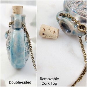 May include: Double-sided, light blue ceramic flask with a removable cork top. The flask has a floral design and a brass chain. The text "Double-sided" and "Removable Cork Top" are visible in the image.