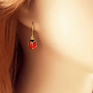 May include: Gold ladybug earrings with red and black enamel. The earrings are dangle style with a simple hoop.