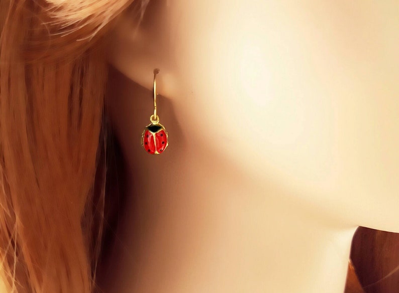 May include: Gold ladybug earrings with red and black enamel. The earrings are dangle style with a simple hoop.