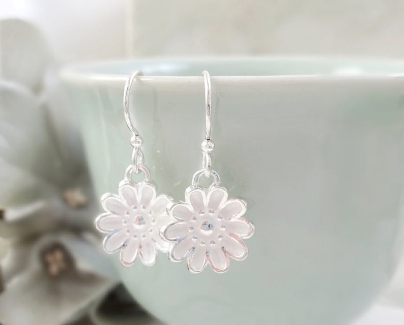 May include: A pair of silver dangle earrings with white flower charms. The flowers have a delicate, detailed design.