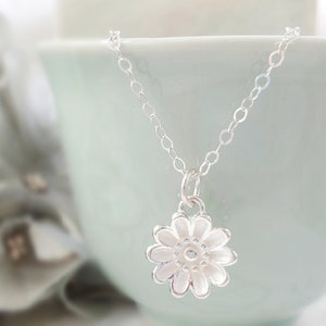 May include: A silver chain necklace with a delicate silver flower pendant. The flower has a textured surface and a small center.