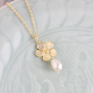 May include: A gold chain necklace with a delicate flower pendant and a single pearl drop.