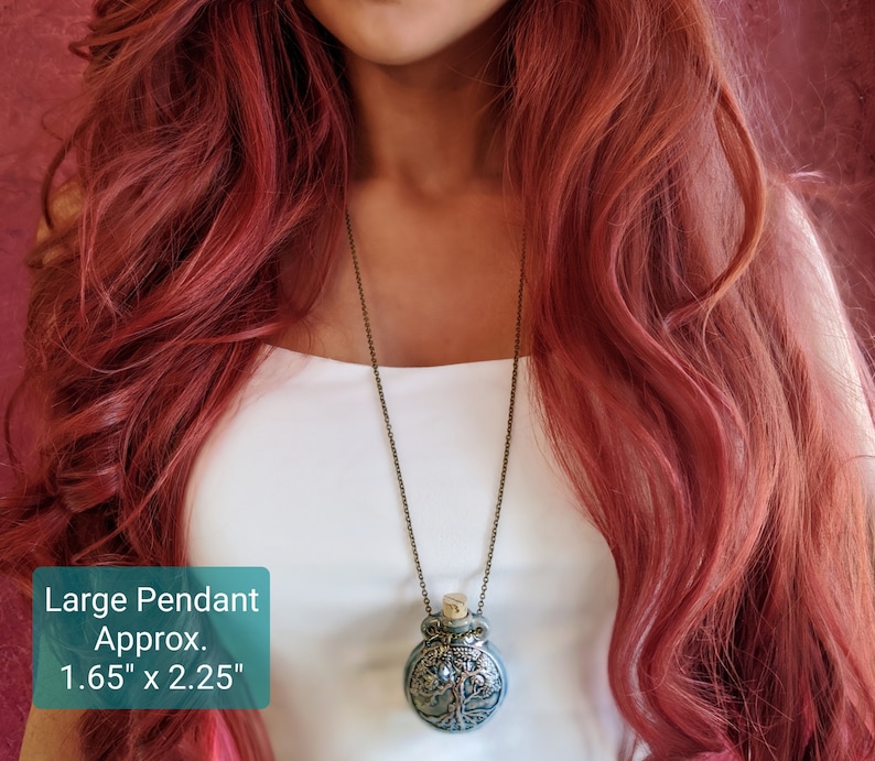May include: A large pendant necklace with a detailed tree of life design. The pendant is approximately 1.65 inches wide and 2.25 inches tall, with a cork stopper. The chain is a dark bronze color.