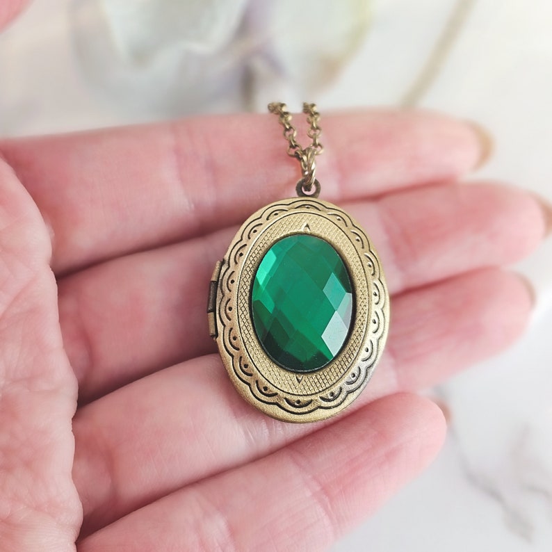 Puede incluir: Un collar con un medall&oacute;n ovalado de oro adornado con una piedra preciosa verde. El medall&oacute;n tiene un dise&ntilde;o ornamentado detallado alrededor del borde.