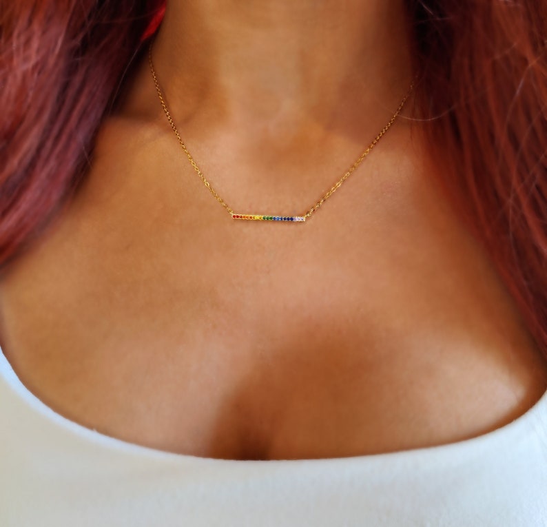May include: A gold chain necklace with a thin bar pendant featuring a rainbow of colorful cubic zirconia stones.