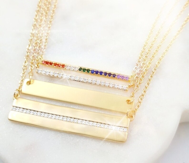 May include: Gold layered necklace with a bar pendant featuring a row of colorful gemstones and a double row of clear cubic zirconia stones.