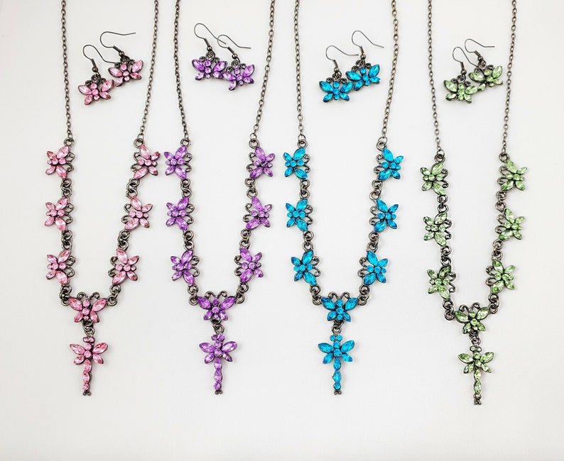 Puede incluir: Cuatro collares con dijes de mariposa y aretes a juego. Los collares son plateados con mariposas de cristal rosa, morado, azul y verde. Los aretes son plateados con mariposas de cristal a juego.