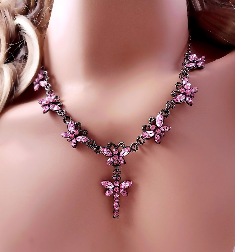 Puede incluir: Un delicado collar de mariposa de cristal rosa con un colgante de mariposa colgante. El collar est&aacute; hecho de metal negro y presenta una cadena con m&uacute;ltiples abalorios de mariposa.