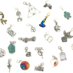 May include: A collection of silver-toned and colorful charms with lobster claw clasps. Charms include a cat, a four-leaf clover, a wizard hat, a rainbow, a cassette tape, a Buddha head, a heart, a unicorn, a sewing machine, and a tie-dye design.