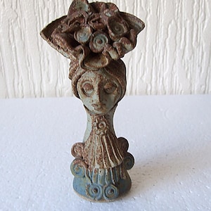 Peut inclure: Une figurine en céramique d'une femme avec un glaçage bleu et brun. Elle porte un chapeau avec des fleurs sur le dessus. La figurine mesure environ 15 cm de haut.