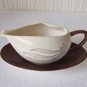 Peut inclure: Un saucier en céramique blanche avec une anse brune et un motif abstrait brun et blanc. Le saucier est posé sur une soucoupe brune assortie.