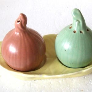 以下が含まれることがあります： セラミック製の塩コショウ入れセット。塩入れは赤茶色、コショウ入れは緑色です。どちらも玉ねぎの形をしており、黄色の葉の形をしたお皿の上に置かれています。キッチン用品です。