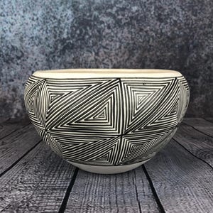 Puede incluir: Un cuenco de cerámica blanca con un patrón geométrico negro de triángulos. El cuenco está sobre una superficie de madera.