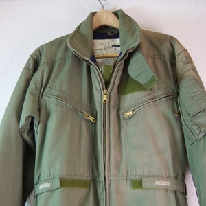 May include: A green flight suit with a zipper closure and multiple pockets. The suit has "MUSTANG" written on the legs and "AVIATION SURVIVAL GEAR" on the chest.