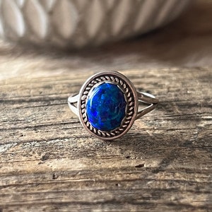 May include: A silver ring with a blue opal gemstone set in a rope-like border.