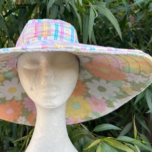 May include: A wide-brimmed sun hat with a pink and blue plaid crown and a floral print lining. The hat is made of a soft, lightweight fabric.