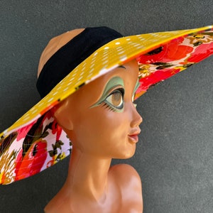 May include: A wide-brimmed sun hat with a yellow polka dot pattern on the top and a floral pattern on the underside. The hat has a black band around the crown.
