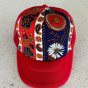 May include: A red and blue trucker hat with a floral pattern. The hat has a mesh back and a solid red front.