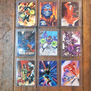 Peut inclure: Neuf cartes de collection de bandes dessinées dans des pochettes de protection. Les cartes présentent des illustrations colorées de divers super-héros et méchants. L'œuvre d'art comprend des personnages en poses d'action, avec des arrière-plans vibrants et des compositions dynamiques.