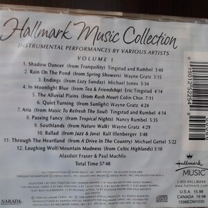 May include: The back of a CD case for the Hallmark Music Collection, Volume 1. The case is white with black text listing the 12 instrumental tracks on the CD, including the title, artist, and album from which the song originates. The case also includes the total time of the CD, 57:48, and the names of the producers, Alasdair Fraser and Paul Machlis. The case has a barcode and a Hallmark Music logo.