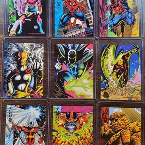 Op de afbeelding: Een verzameling van negen trading cards met verschillende superhelden en superschurken. De kaarten zitten in een doorzichtige plastic hoes en hebben een holografische afwerking. De personages zijn onder andere Spider-Man, Storm, Thanos, The Thing, en meer.