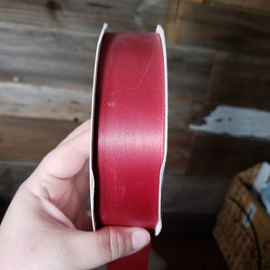 Könnte beinhalten: Eine Rolle rotes Satinband auf einer weißen Pappspule.