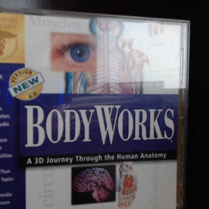 以下が含まれることがあります： 「BODY WORKS」のCD-ROMケース。人体の解剖学を3Dで旅する。表紙には目、骨格系と筋肉系、脳のイラストが描かれています。「NEW VERSION 6.0」と「Medical Library」のブランドが含まれています。