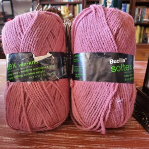May include: Two skeins of pink yarn, one labeled "Bucilla Softex" and the other "Tex Win-Knit". Both skeins are 100% acrylic and are 4-ply knitting worsted weight.