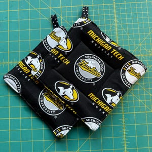 May include: Two black and yellow pot holders with the text "Michigan Tech Huskies" and a husky dog logo.