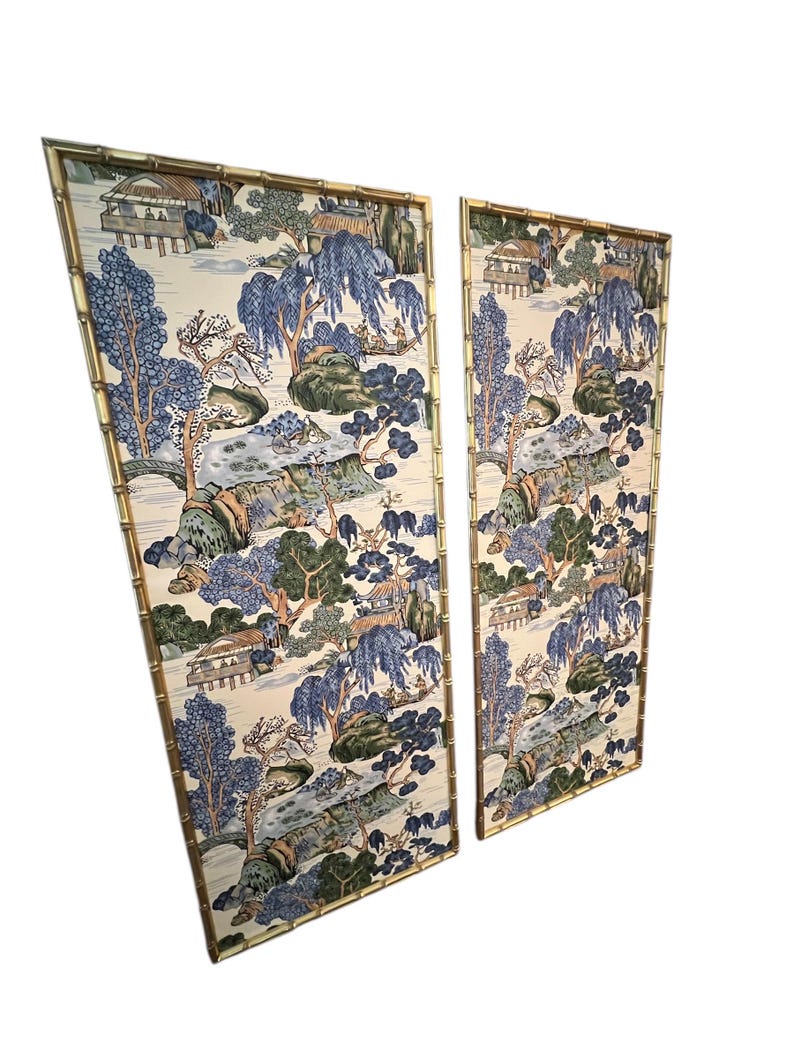 May include: Two decorative wall panels with a bamboo-style gold frame. The panels feature a scenic landscape design with blue, green, and beige tones. The artwork depicts trees, buildings, and water features, creating a serene aesthetic.
