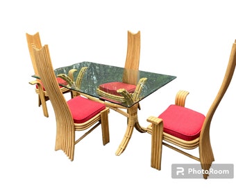 May include: A dining set featuring a rectangular glass-top table and four chairs. The chairs have red cushions and curved, light-colored bamboo frames. The table base is also bamboo. The set is designed for indoor use.