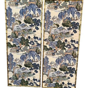 May include: Two rectangular wall panels with a bamboo-style gold frame. The panels feature a scenic landscape design in shades of blue, green, and beige, depicting trees, houses, and water features. The overall aesthetic is reminiscent of traditional Asian art.
